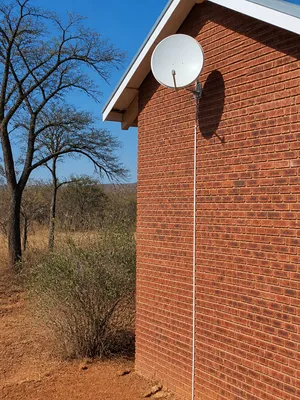 Satellite dish wall-mounted on a face-brick home with bushveld behind