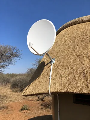 Satellite dish mounted at the edge of a thatched roof in the bushveld